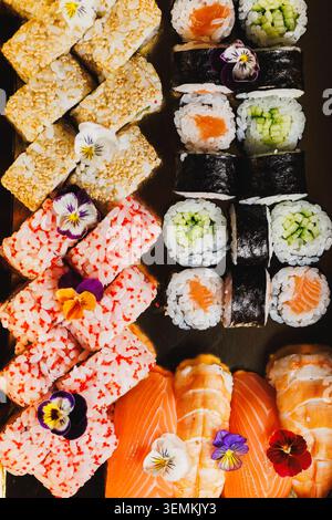 Una collezione di sushi roll e sashimi è collocata su un piatto nero. Diversi tipi di sushi sono disposti in modo ordinato con elementi decorativi. Si Foto Stock