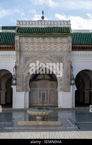 Il cortile della Madrasa al-Attarine presenta una porta ornata ad arco, intricate piastrelle, intonaco intagliato e tegole verdi sotto un cielo blu. Foto Stock