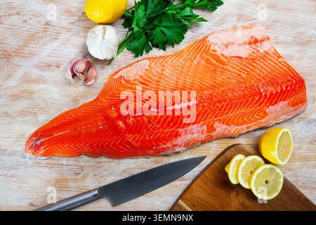 Filetto di salmone crudo su tavola di legno con condimenti Foto Stock