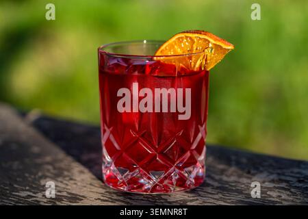 Classico cocktail negroni con ghiaccio e fetta di arancia secca. Rinfrescante cocktail campari alcolico rosso rubino con cubetti di ghiaccio servito in un esterno di cristallo Foto Stock