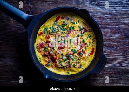 Frittata con pomodori e erba cipollina in padella, primo piano. Vista dall'alto di una deliziosa frittata calda con pomodori rossi e cipolle verdi fresche servite Foto Stock