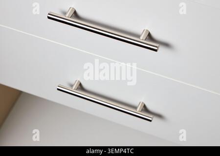 Primo piano di mobili in legno bianco con due eleganti maniglie con barra a T in acciaio inox montate orizzontalmente sulle moderne facciate dei cassetti per un design pulito e minimalista Foto Stock