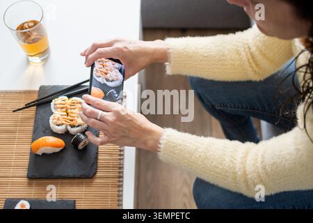 Vista ravvicinata di una persona che gusta sushi e maki assortiti con bacchette a casa. Ambiente accogliente e cucina giapponese, cucina salutare Foto Stock