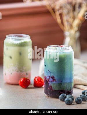 Latticini matcha a strati di mirtilli e fragole in bicchieri a forma di lattina con frutti di bosco freschi. Foto Stock