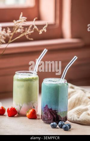 Latticini matcha a strati di mirtilli e fragole in bicchieri a forma di lattina con frutti di bosco freschi. Foto Stock