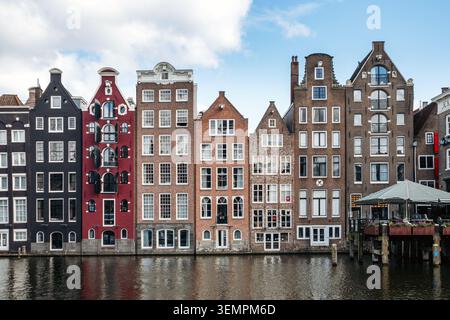 Amsterdam, Paesi Bassi - 20 aprile 2026: Tradizionali case sui canali lungo il lungomare di Damrak vicino alla stazione centrale di Amsterdam, che si riflettono nella calma Foto Stock