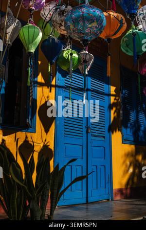 Vivaci lanterne di seta appese davanti ad una porta blu brillante su una facciata gialla dell'edificio storico Foto Stock