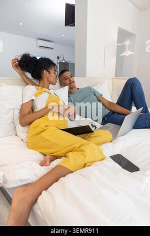 Diverse coppie sdraiate sul letto, donna in tuta di senape con notebook, uomo che usa un computer portatile Foto Stock
