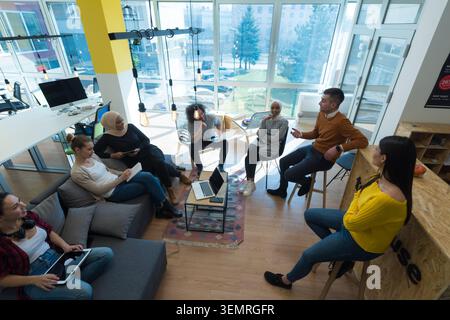 Grandangolo alto che mostra un intero team multietnico di giovani colleghi professionisti che interagiscono, lavorano su notebook e discutono di un progetto in Foto Stock