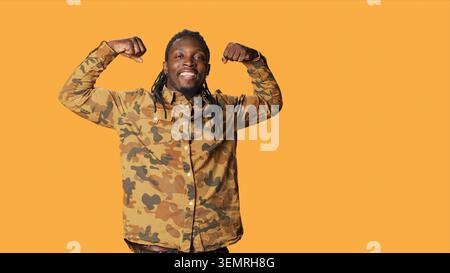 Persona forte che si flette con la fotocamera e mostra il suo fisico tonico, atletico con bicipiti enormi, un ragazzo afroamericano potente che si sente sicuro dopo essere andato in palestra Foto Stock