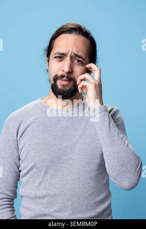 Una persona incerto del Medio Oriente si sente incerta e confusa su sfondo blu, contemplando e sentendosi curiosa in studio Foto Stock