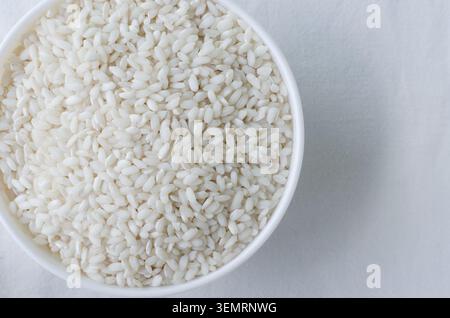 Una ciotola bianca di riso Arborio su sfondo bianco. Concetto di cucina italiana, risotto e alimentazione sana. Riso crudo. Cucina mediterranea. Foto Stock