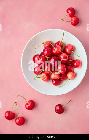 Ciliegie rosse fresche nella ciotola bianca su sfondo rosa, vista dall'alto Foto Stock