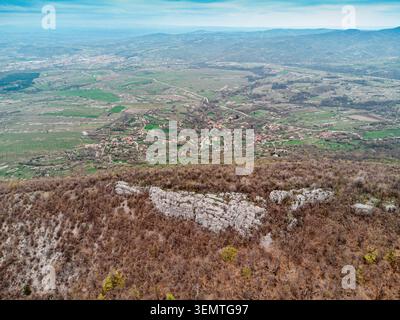 Drone che cattura un vasto paesaggio con un piccolo villaggio annidato tra campi agricoli e colline sotto un vasto cielo Foto Stock