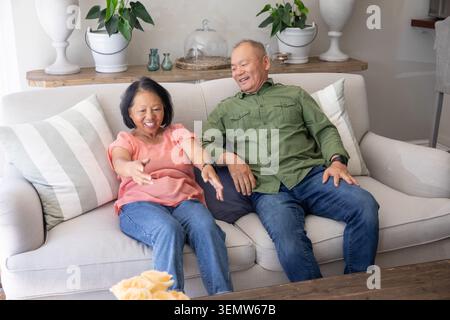 Donna anziana e uomo asiatico maturo seduto sul divano in soggiorno, che si avvicina al bouquet Foto Stock