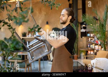 Cameriere maschile che organizza mobili e allestisce caffè Foto Stock