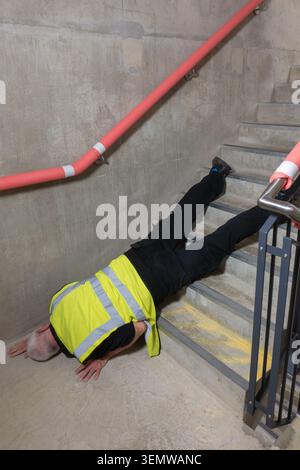 I lavoratori edili maturi inciampano e cadono mentre lavorano su scale in cemento in una nuova costruzione. L'ingegnere senior scivola e cade giù da una rampa di scale W. Foto Stock