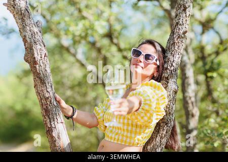 Donna matura rilassata con vino bianco nella Sunny Forest Foto Stock