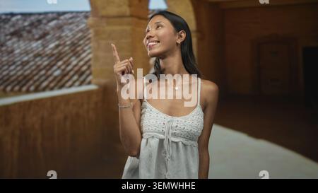 Donna tailandese che punta il dito indice verso l'alto sul tetto piastrellato all'interno di un edificio in pietra; scoperta della curiosità. Foto Stock