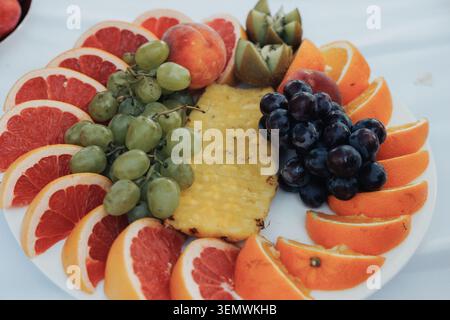 Frutta fresca disposta a pianta circolare. Grappoli di uva, arance e una fetta di ananas. Le fette di pompelmo rosse e rosa aggiungono contrasto. Colorato, vib Foto Stock