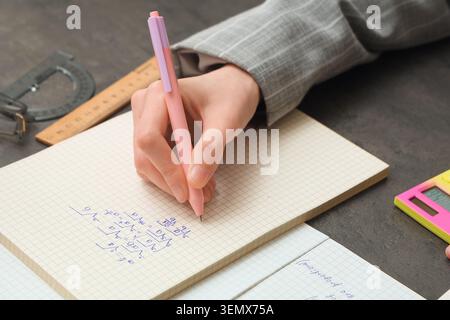 Donna che scrive formule matematiche su un quaderno al tavolo buio, primo piano Foto Stock