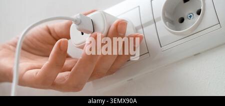 Collegando manualmente il caricabatterie USB bianco alla presa a muro per la ricarica del dispositivo e l'alimentazione, questa azione rappresenta un collegamento elettrico essenziale e un'alimentazione Foto Stock