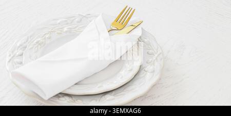Eleganti piatti bianchi con posate e tovagliolo dorati su un tavolo in legno rustico, un tovagliolo in tessuto bianco piegato in modo ordinato contiene un set di lucentezza Foto Stock
