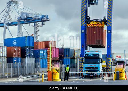 Porto di Auckland a cavallo che carica un container su un camion normanno con operaio in giubbotto ad alta visibilità Foto Stock