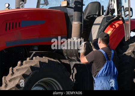 Un operatore del trattore, un agricoltore, estrae o installa un filtro dell'aria nel trattore per pulirlo, spurgarlo o sostituirlo. Manutenzione di macchine agricole in Foto Stock