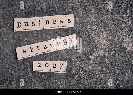 Strategia aziendale 2027 parole sui tagli di carta, disposte su un'area di sfondo in cemento scuro Foto Stock