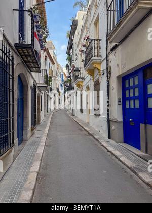 Sitges, Spagna - 13 settembre 2025: Una splendida vista prospettica di una strada acciottolata vuota e stretta fiancheggiata da tradizionali case bianche Foto Stock