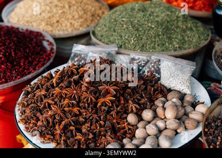 Una vivace e aromatica esposizione di varie spezie, tra cui anice stellato, noce moscata ed erbe macinate colorate, disposte in grandi ciotole e piccoli sacchetti. Questa immagine mostra le ricche tradizioni culinarie di un autentico mercato orientale o bazar. Foto Stock