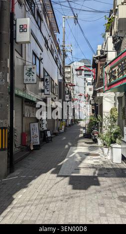 Stretta via commerciale tradizionale immersa nella calda luce del sole, fiancheggiata da negozi e insegne giapponesi a Osaka, Giappone Foto Stock