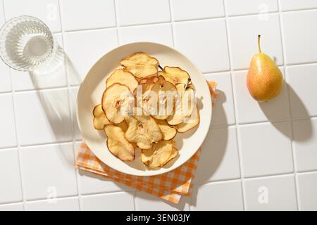 Frutta patatine e acqua in piena ombra su uno sfondo bianco piastrellato. Dessert vegano senza zucchero. Vista dall'alto. Spazio di copia. Foto Stock