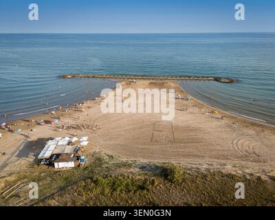 Vista aerea di una spiaggia sabbiosa con persone sparse e una piccola struttura sulla spiaggia. Foto Stock