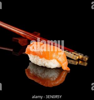 Sushi fresco al nigiri di salmone su una superficie lucida nera riflettente con bacchette di legno e riflessi a specchio. Foto Stock