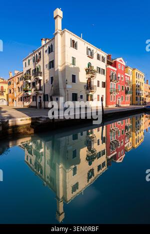 Edifici colorati si riflettono in un canale calmo in una giornata di sole con cielo blu. Foto Stock