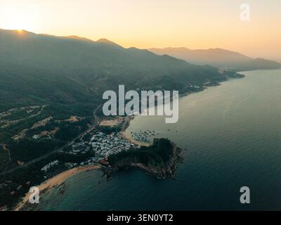 Vista aerea del villaggio sul mare e della costa al tramonto, con montagne e oceano in vista. Foto Stock
