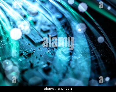 Primo piano di un circuito stampato con fibre luminose e una futuristica tonalità blu-verde. Foto Stock
