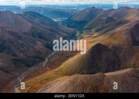 Maestosa vista aerea delle aspre montagne e di un fiume tortuoso sotto un vasto cielo blu. Foto Stock