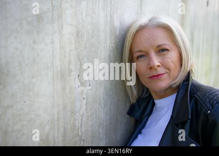 Donna matura con capelli biondi corti appoggiati a una parete di cemento testurizzato. Foto Stock