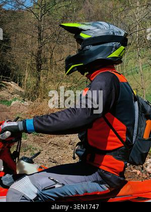 Guida fuoristrada che indossa casco e attrezzatura protettiva su Red Dirt Bike in Forest Trail Foto Stock