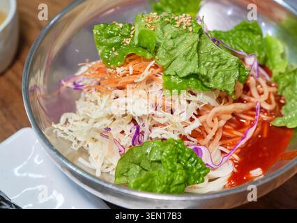 Tradizionale zuppa coreana di spaghetti caldi, un rotolo di riso alle alghe e spaghetti misti speziati con verdure fresche serviti in autentiche ciotole in acciaio inox. Foto Stock