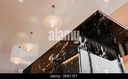 Moderna cucina a soffitto con eleganti lampadari pendenti e bancone isolano in marmo scuro. Foto Stock