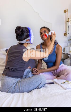 Fornitore e cliente donna a letto, fornitore che indossa una maschera a LED che applica un dispositivo a luce rossa con il telefono Foto Stock