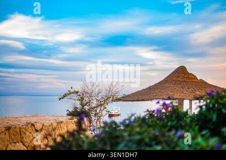 Una vista tranquilla del Mar Rosso a Sharm El Sheikh, Egitto, con un ombrellone tradizionale in paglia e una barca in lontananza Foto Stock