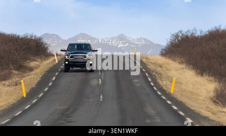 Veicolo che procede su una strada rurale panoramica con montagne innevate nella natura selvaggia dell'Islanda Foto Stock