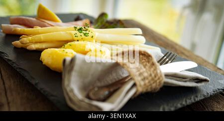 Asparagi bianchi di stagione con cremosa salsa hollandaise, serviti su un piatto di ardesia. Foto Stock