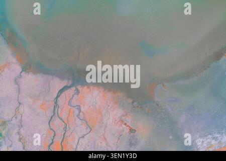 Texture di terra rosa brillante con linee complesse di erosione dell'acqua e depositi minerali accanto a un serbatoio profondo, che sottolineano i cambiamenti ecologici in una fotografia aerea densa e ricca. Foto Stock