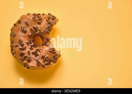 Amalgamare la ciambella al cioccolato con glassa lucida e gocce di cioccolato su sfondo giallo brillante. Composizione minima del cibo con colori vivaci e grande copia spa Foto Stock